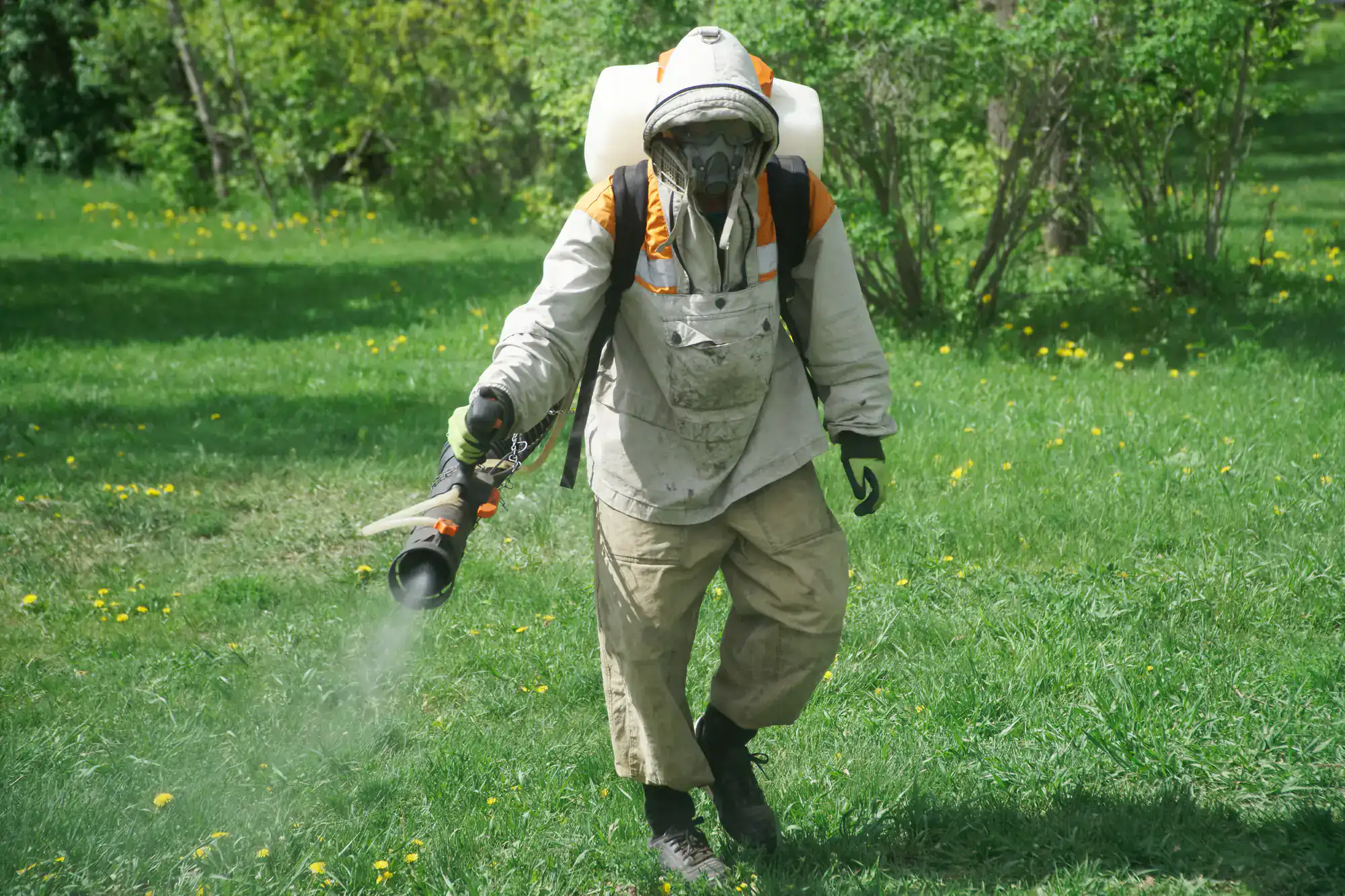 A person in protective gear sprays chemicals on a lawn, suitable for Lawn Renovation Suffolk County needs.
