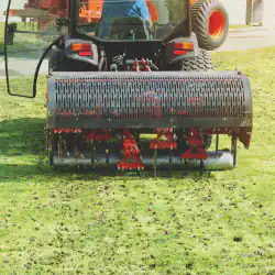 A tractor-mounted lawn aerator perforates grass on a sunny day, aiding Lawn Renovation Suffolk County.