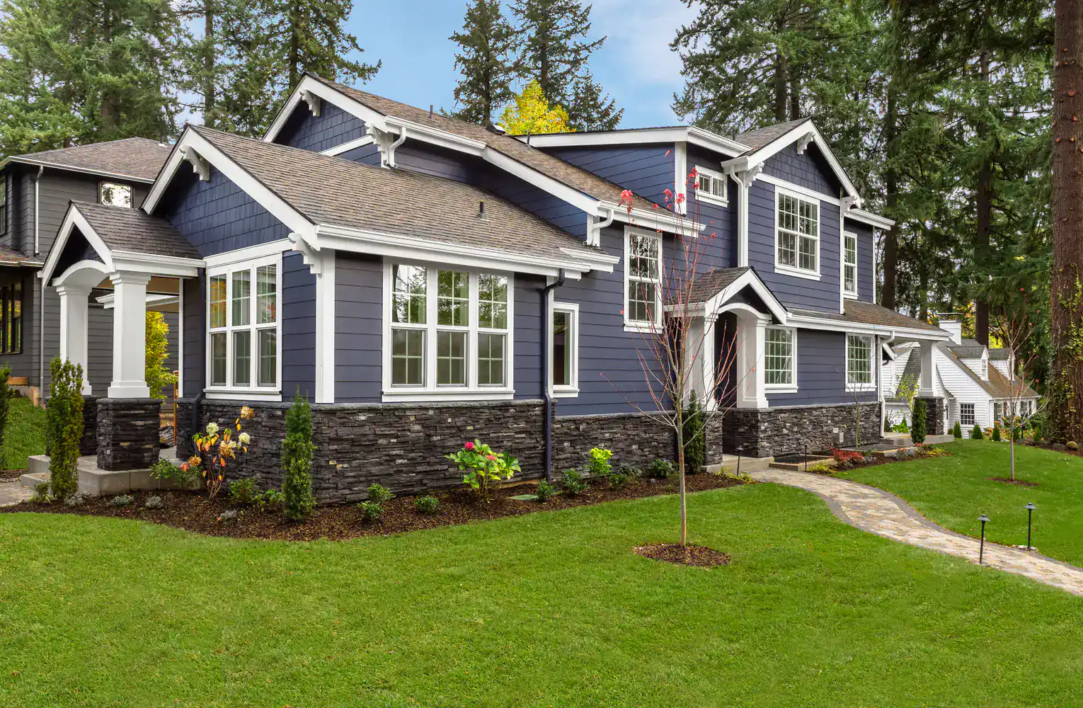 Two-story modern house with dark blue siding, white trim, stone accents, and a landscaped front yard.