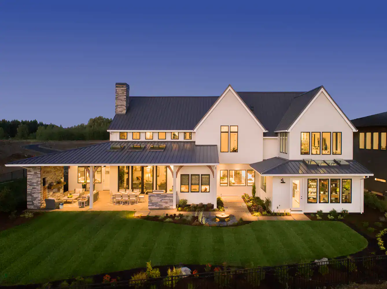 A modern two-story house with large windows, outdoor patio, and pristine lawn is shown at dusk.